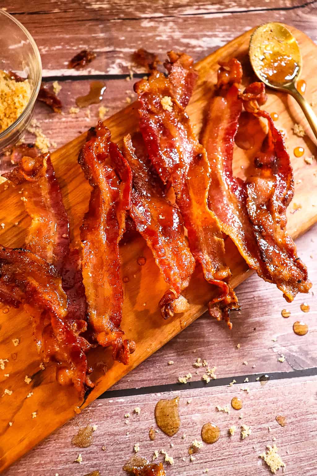 candied bacon laid out on a cutting board with a bowl of brown sugar next to it that is used as a photo prop