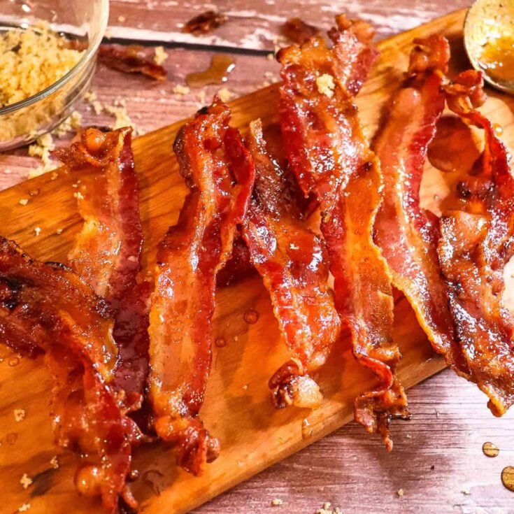 candied bacon laid out on a cutting board with a bowl of brown sugar next to it that is used as a photo prop