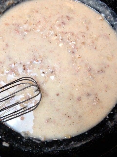 A bowl of prepared Savory Bacon Gravy with a whisk in the mixture.