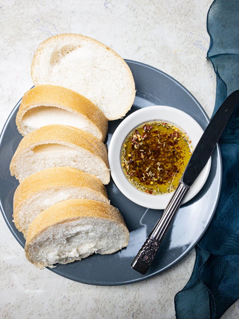 herb infused olive oil bread dip in a bowl on a grey plate with bread next to it