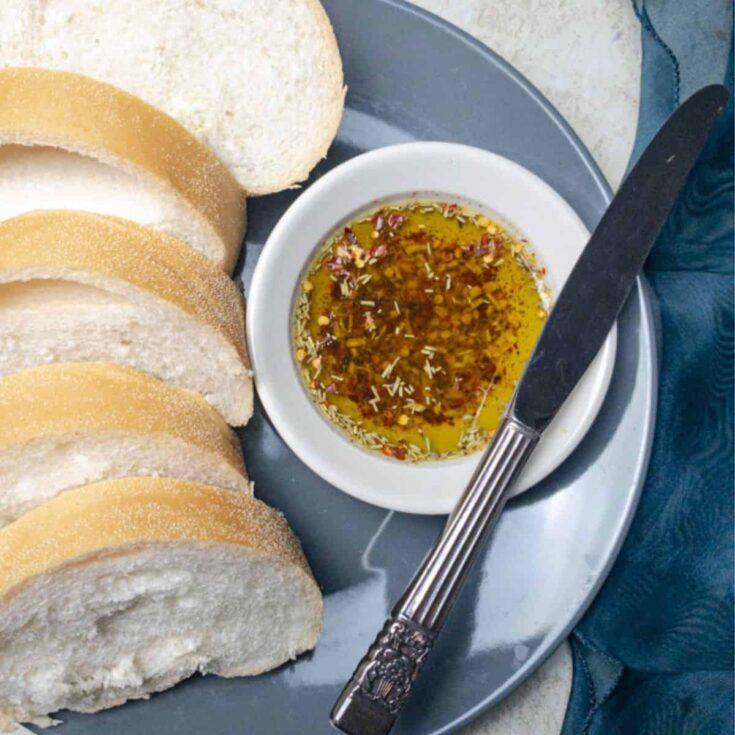 herb infused olive oil bread dip in a bowl on a grey plate with bread next to it