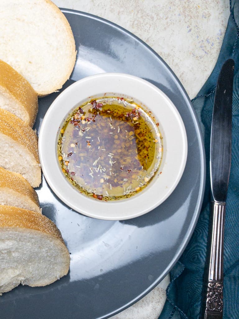 herb infused olive oil bread dip in a bowl on a grey plate
