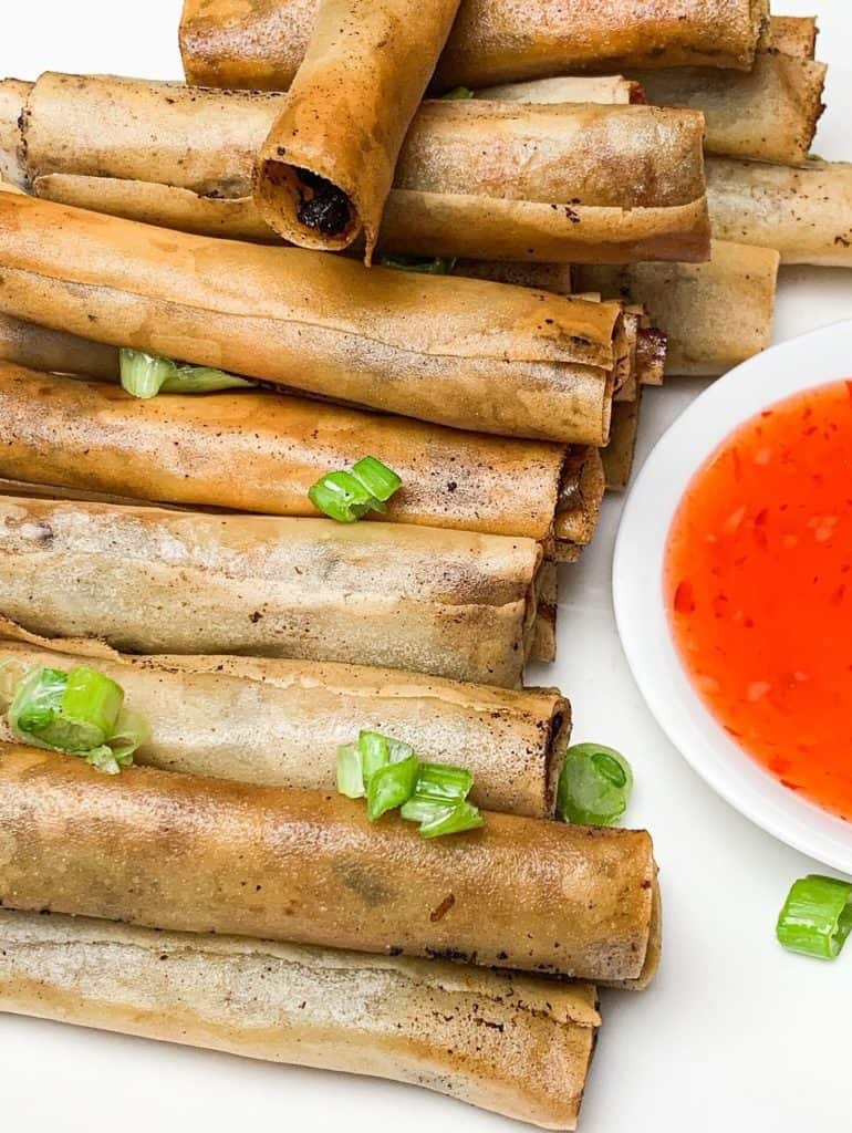 close up view of lumpia beside a dish of sweet chili sauce