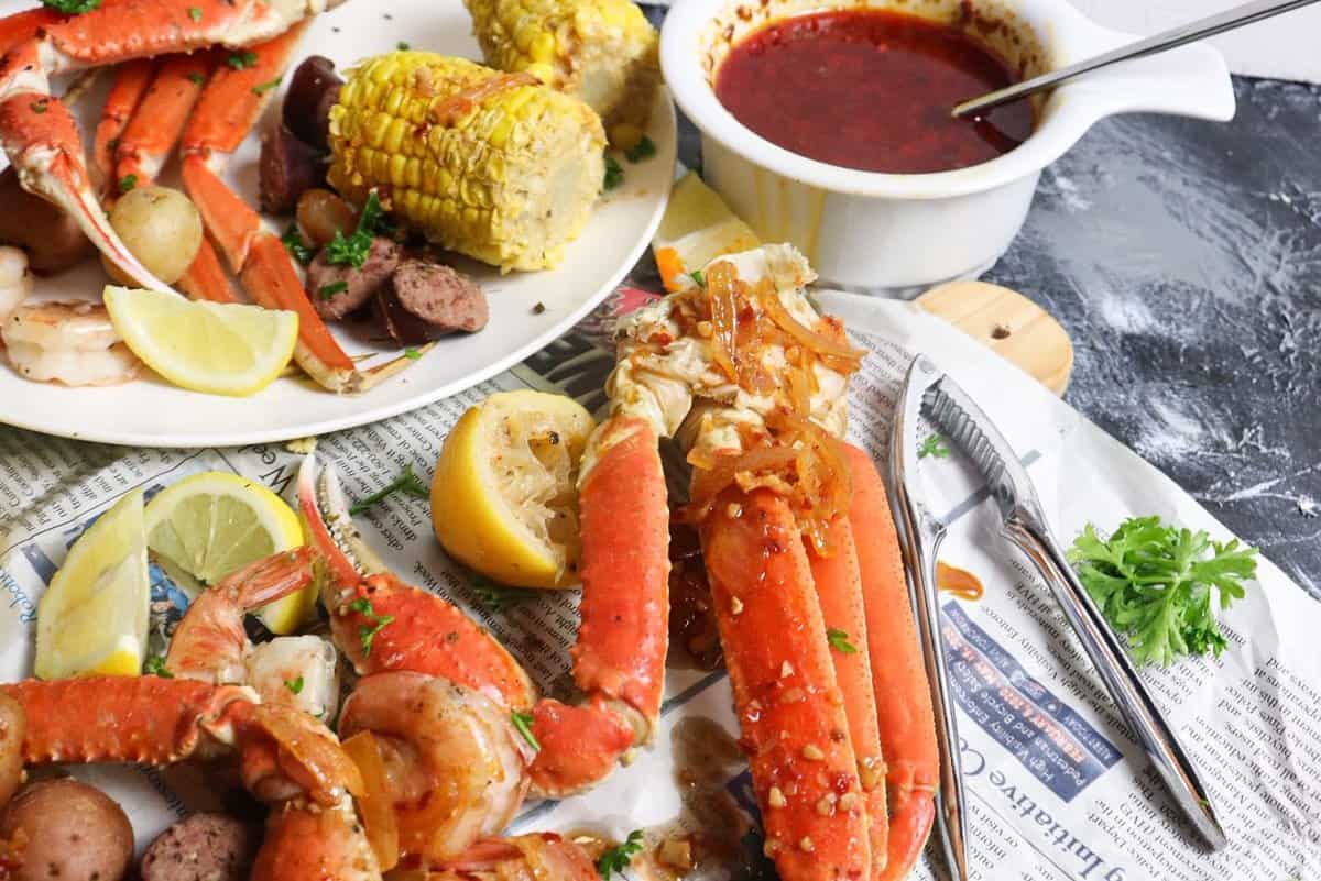 crab legs shrimp and corn on the cob and sausage sitting on a bed of newspaper for a seafood boil