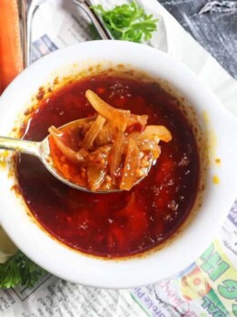 spoon full of cajun seafood boil sauce in a white bowl with crab legs next to it