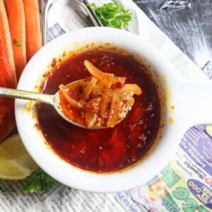 spoon full of cajun seafood boil sauce in a white bowl with crab legs next to it
