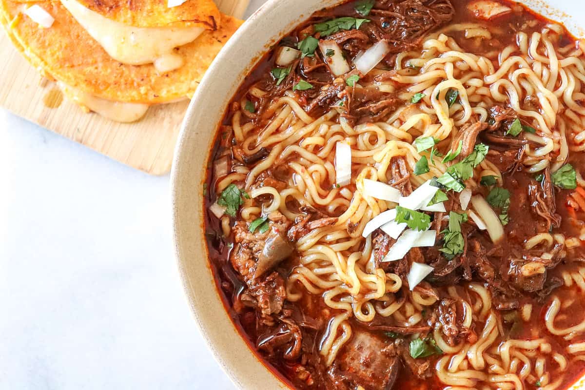 birria ramen in a bowl with quesadillas on the side