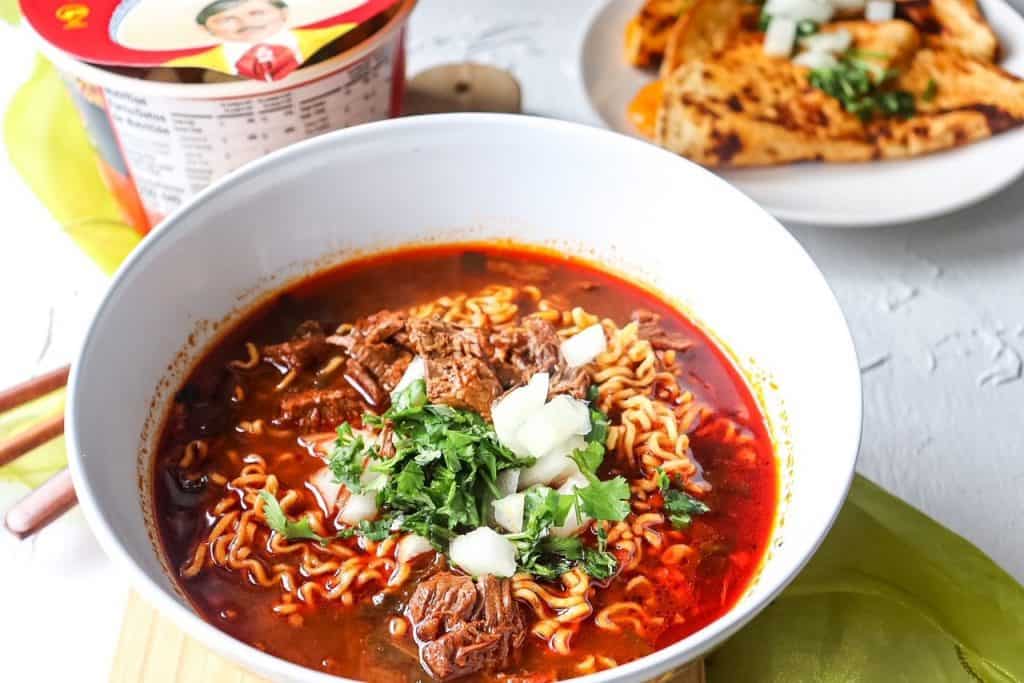 angled shot of birria ramen and cheese quesadillas in the background