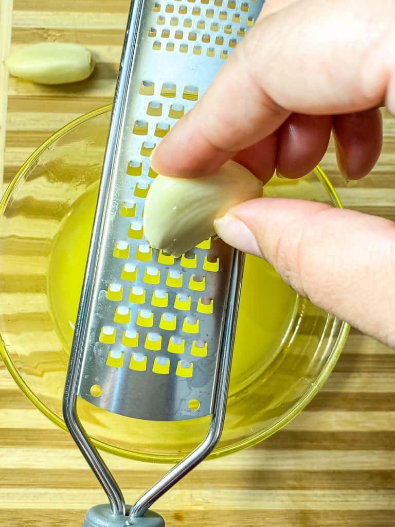 grating garlic over a bowl of melted butter