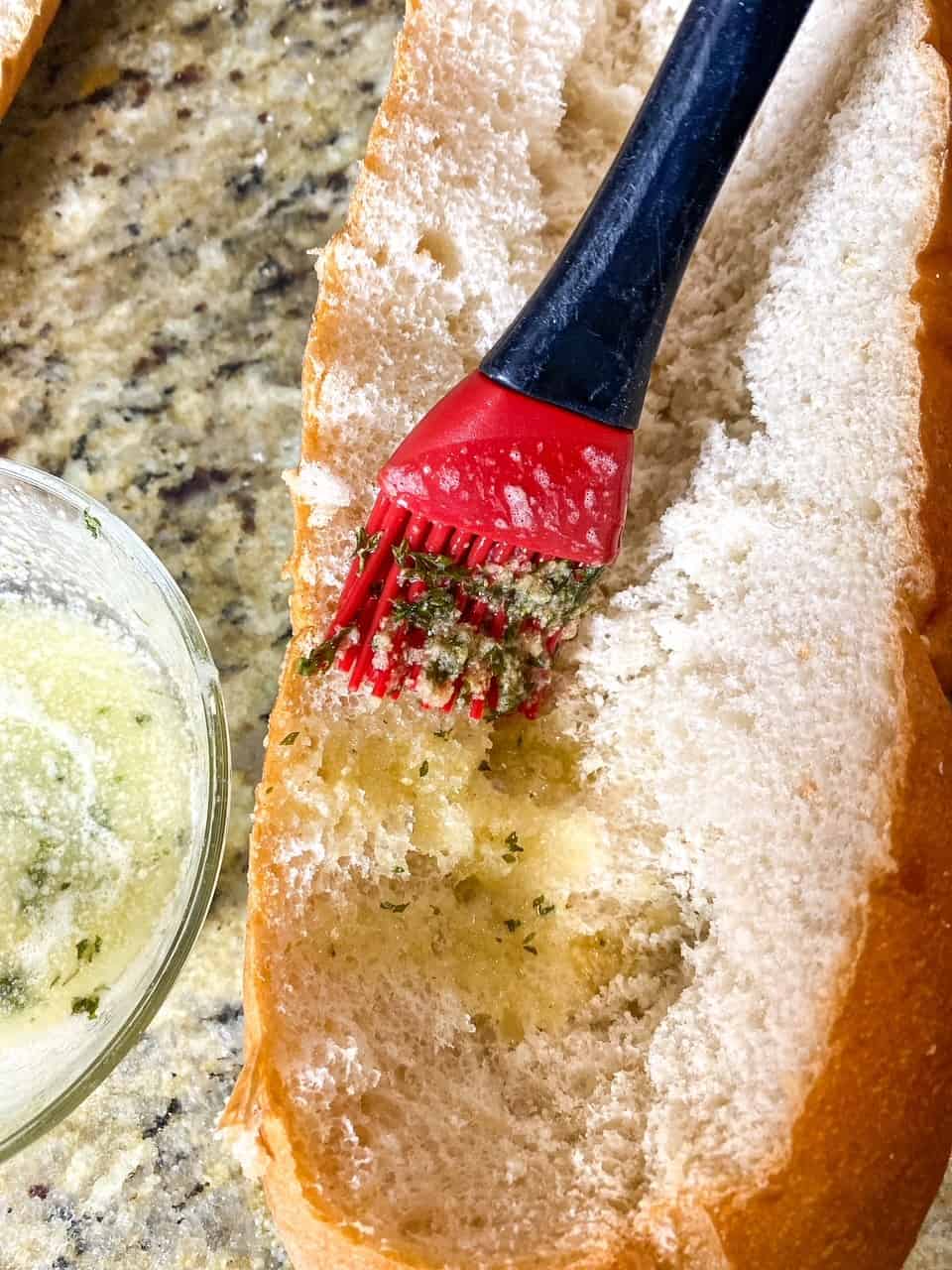 brushing garlic butter onto hollowed out loaf of bread