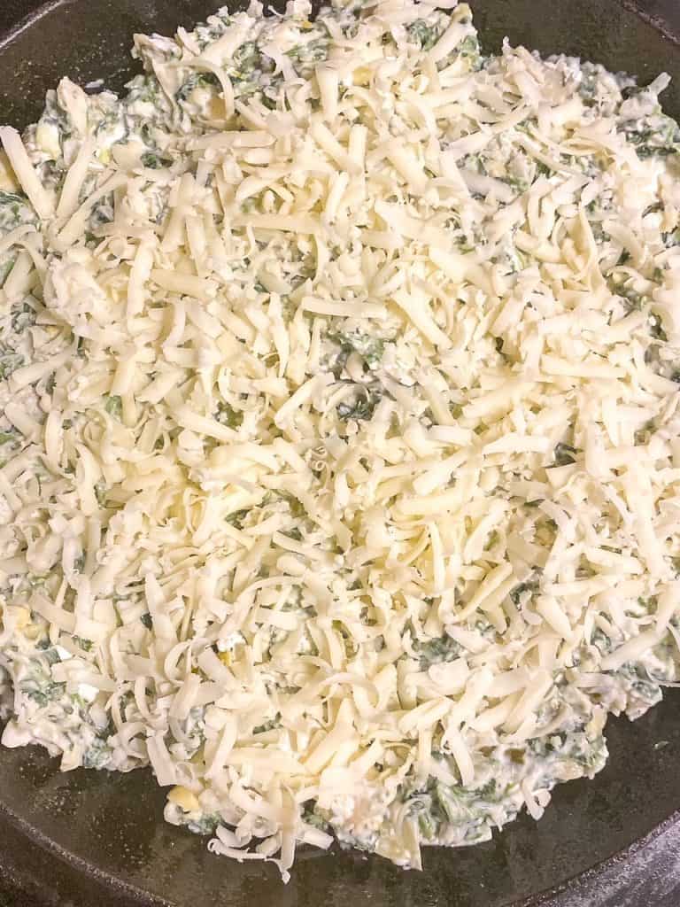 spinach dip that is ready to go in the oven with shredded cheese on top