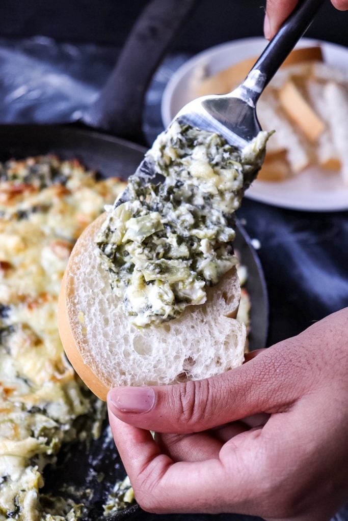 spreading spinach dip onto a piece of bread