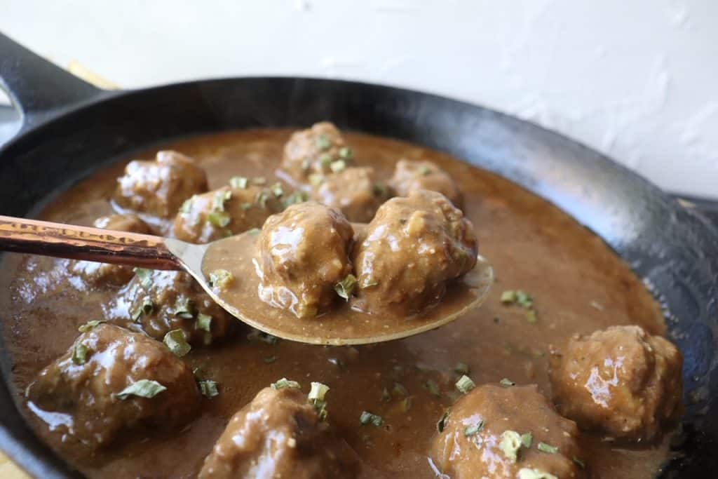 a spoonful of Swedish meatballs over a skillet full of meatballs and broth