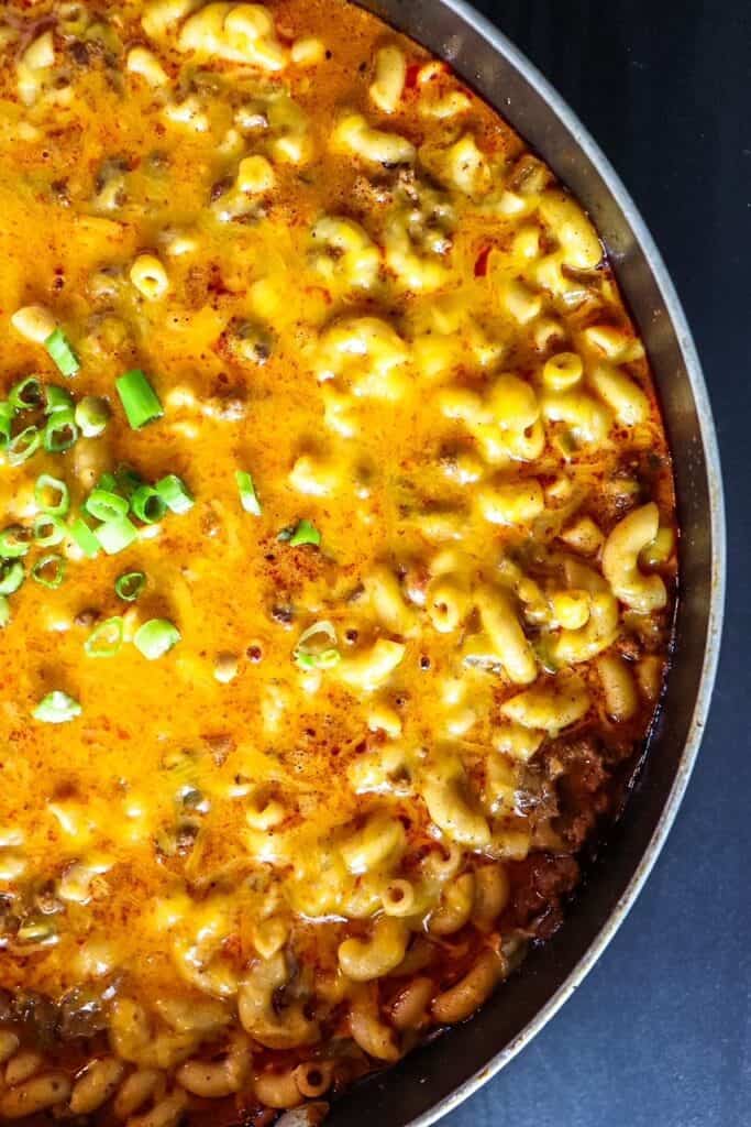 A close up shot of half a pot of Chili Mac and Cheese garnished with scallions.