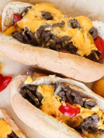 cheese steak sandwiches on a tray with peppers and cheese around them