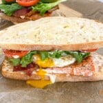 blackened salmon BLT sandwich on a cutting board with egg yolk dripping out
