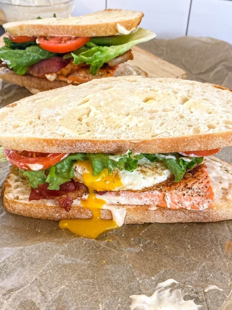 blackened salmon BLT sandwich on a cutting board with egg yolk dripping out