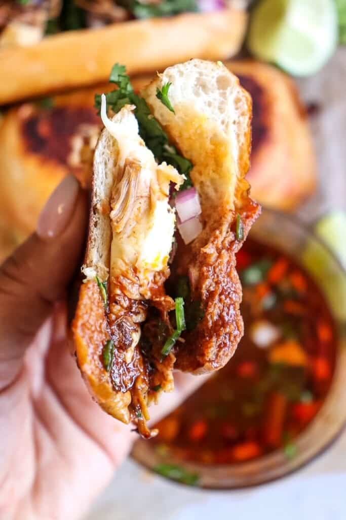 dipping chicken birria grilled cheese sandwiches into the consome sauce