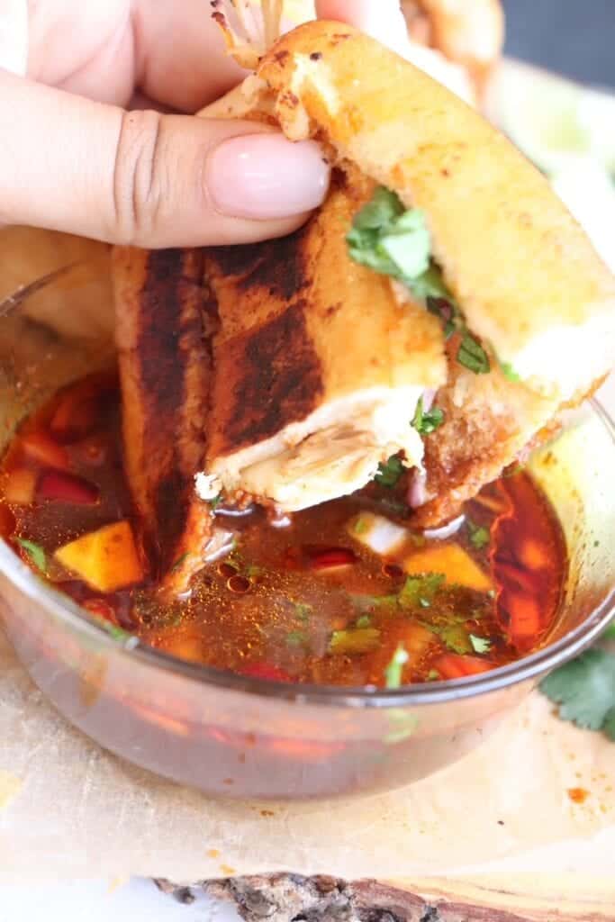 dipping chicken birria grilled cheese sandwiches into the consome sauce