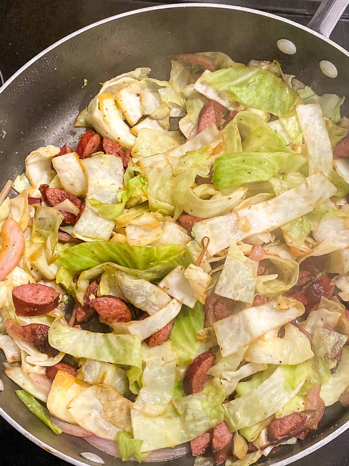 fried cabbage and smoked sausage simmering in a skillet