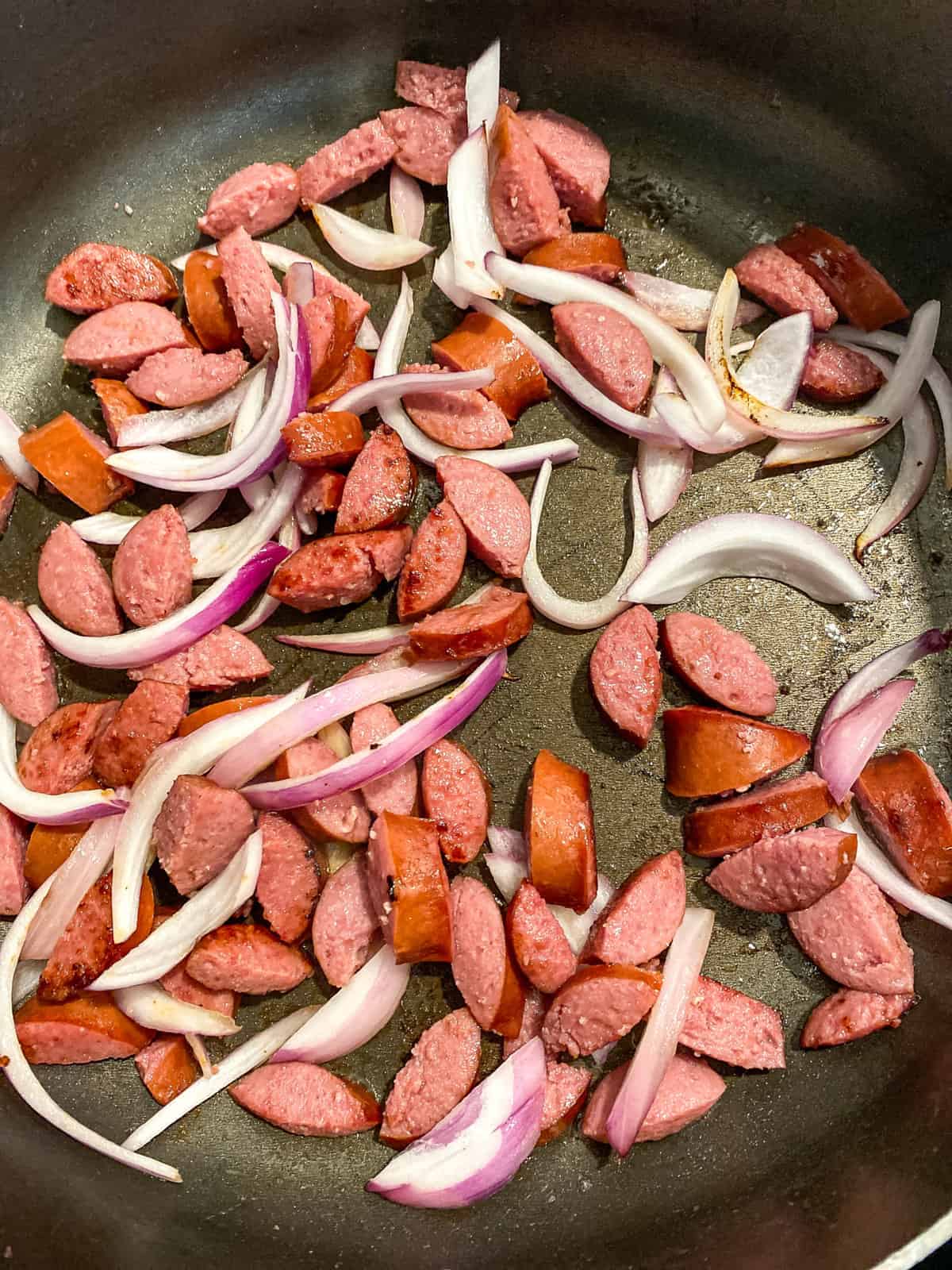 frying beef sausage and onions in a skillet to make fried cabbage