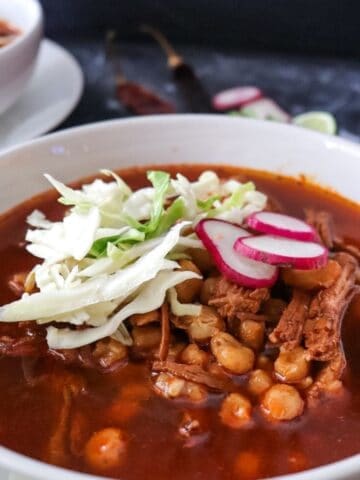 close-up of pozole rojo in a white bowl garnished with cabbage and radish