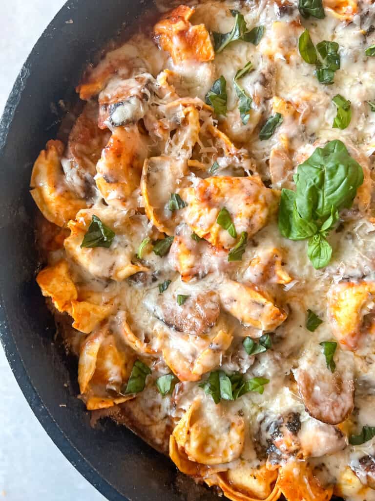 Italian sausage and tortellini with melted cheese on top in a cast iron skillet