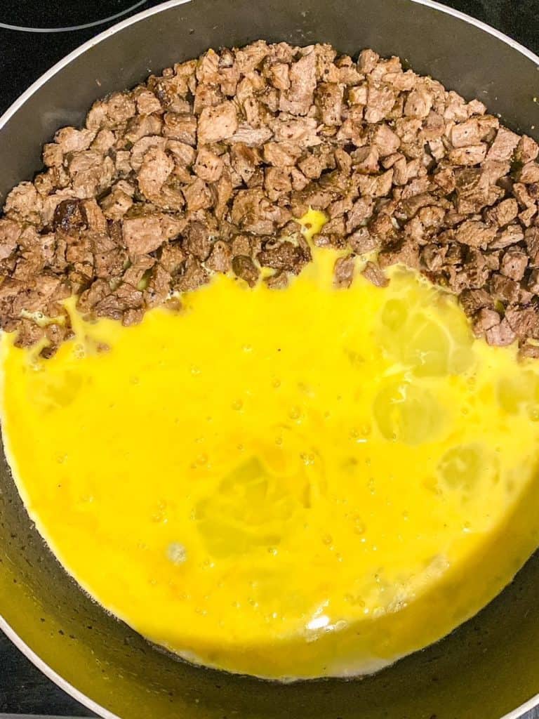 A skillet filled with cut up steak and eggs.