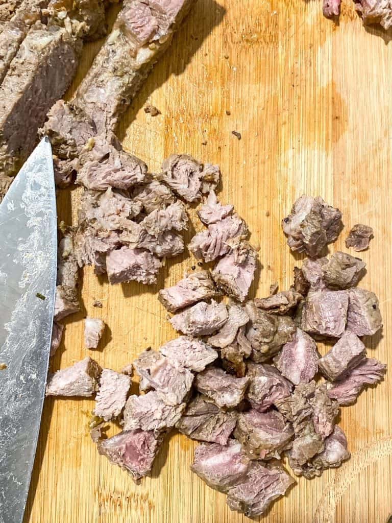 Bite size chunks of steak on a wooden cutting board with a knife beside it.
