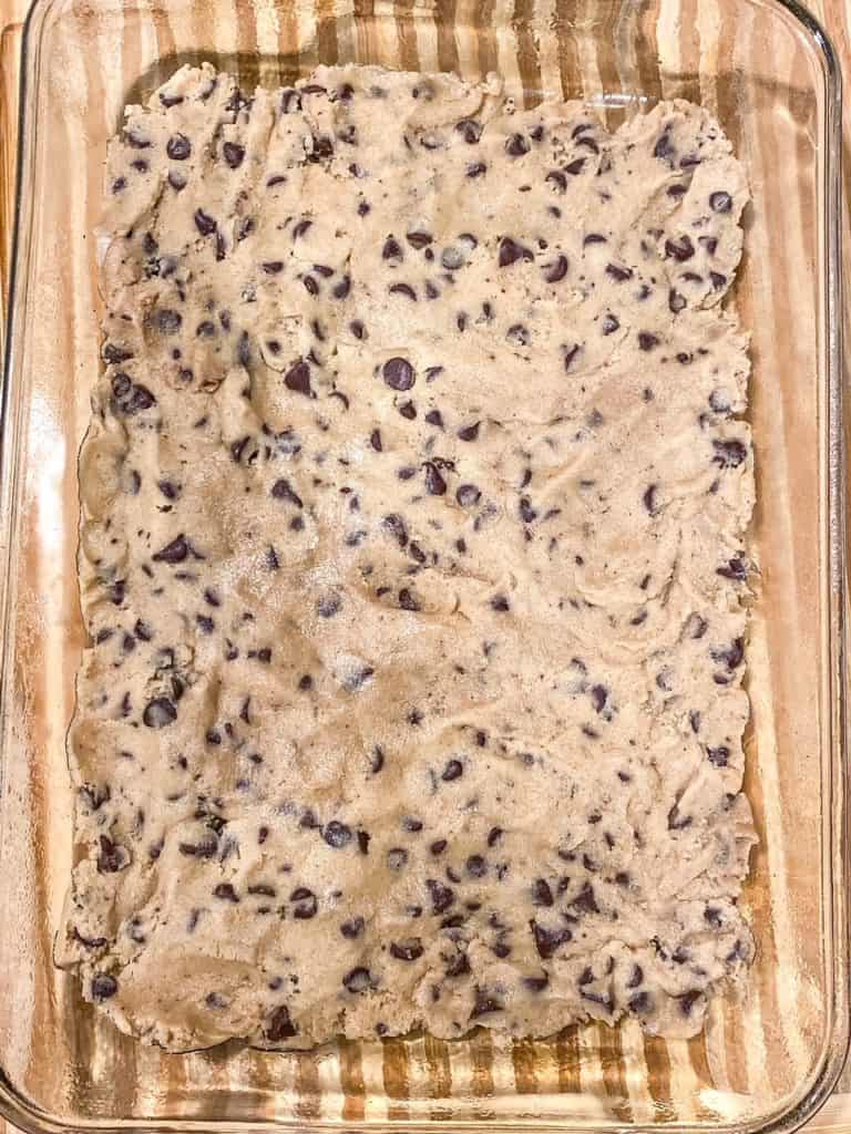 A layer of chocolate chip cookie dough placed at the bottom of a baking dish.