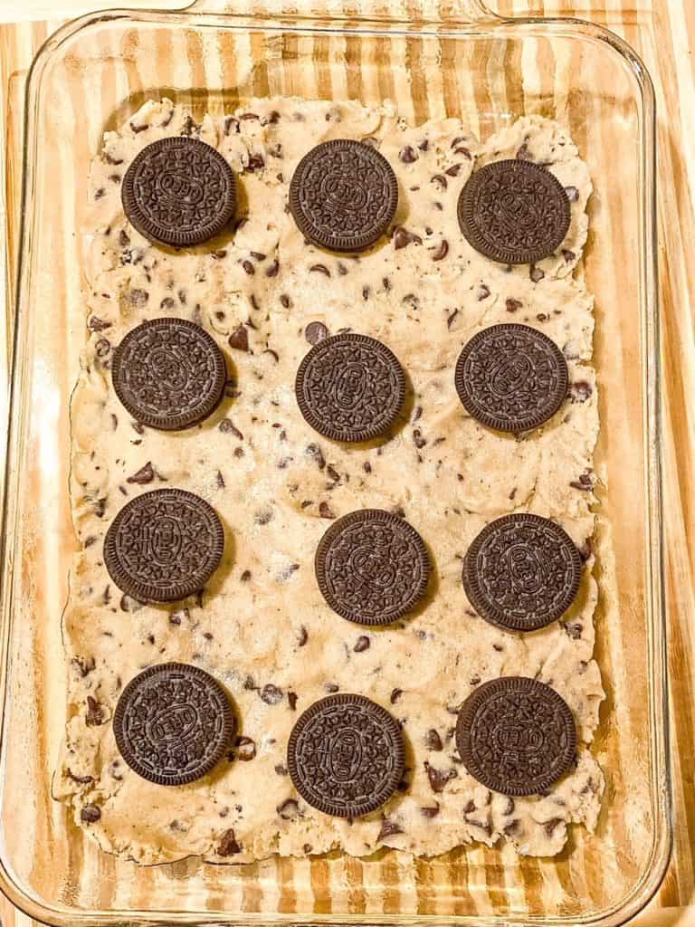 A layer of 12 Oreos placed over a layer of chocolate chip cookie dough in a baking dish.