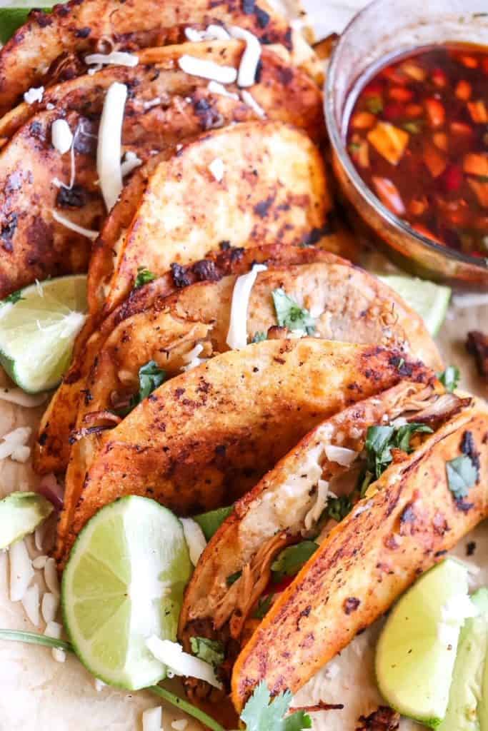 chicken birria quesatacos on a board with lime wedges and consome