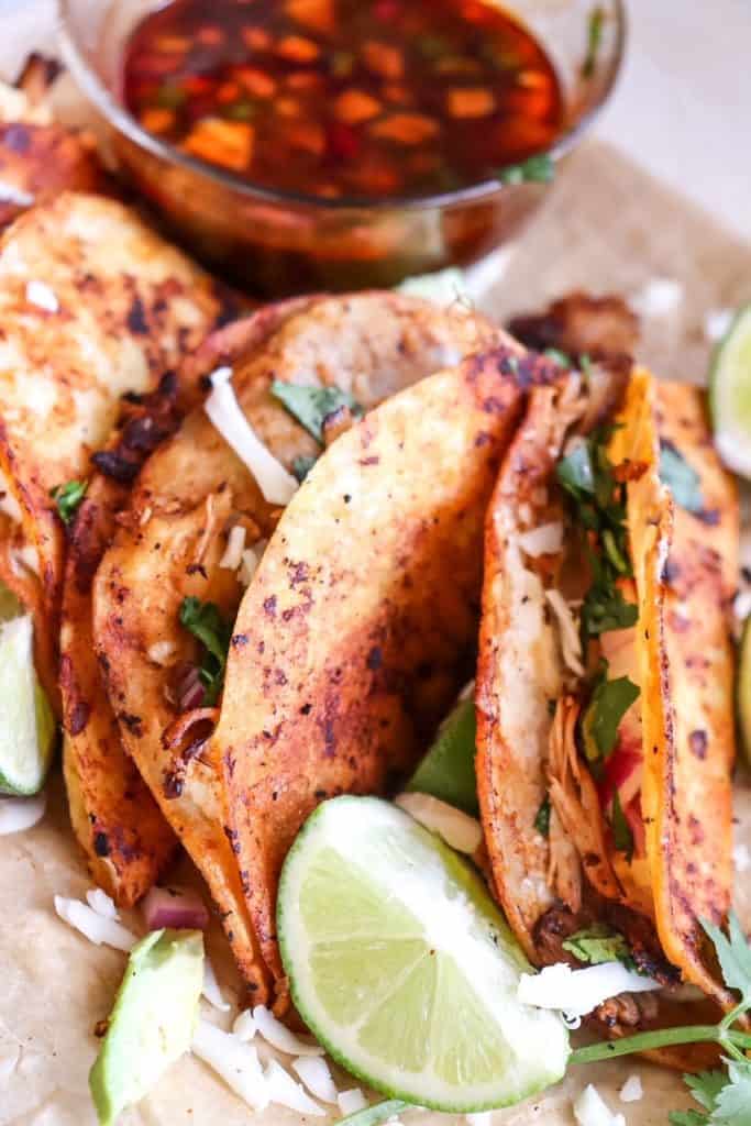 chicken birria quesatacos on a board with lime wedges and consome