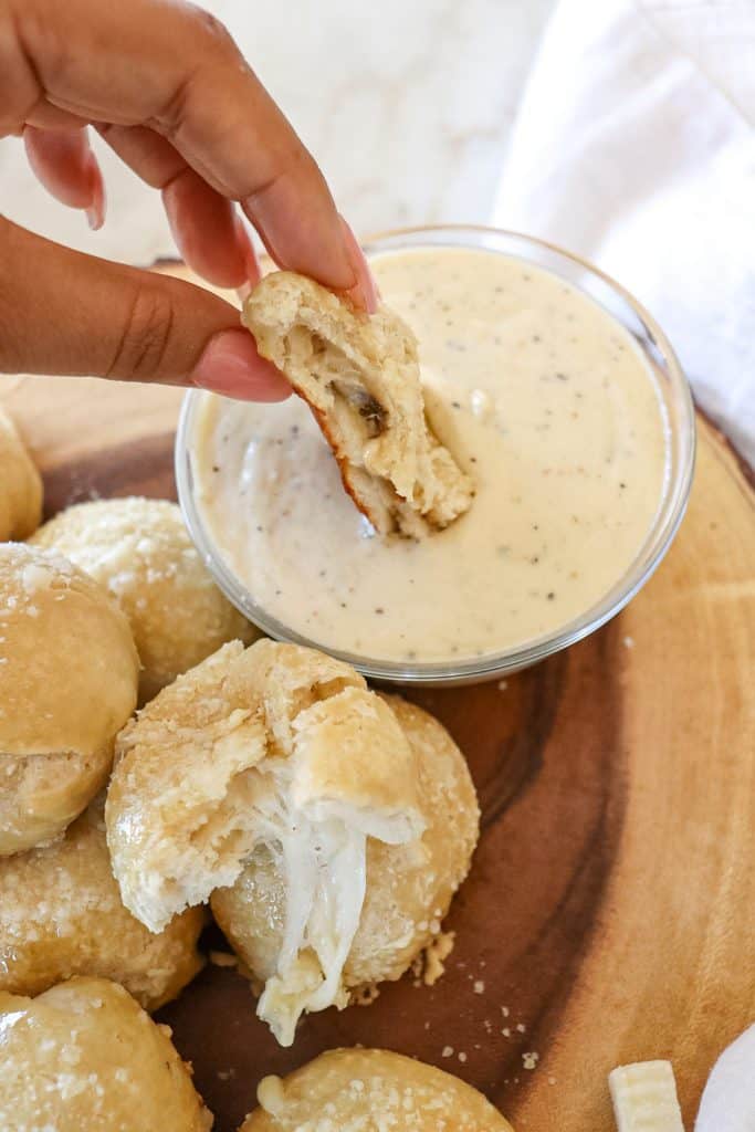 cheese-stuffed pretzel bite cut in half so the cheese in the center is visible being dipped in cheese dip