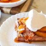 a piece of peach cobbler stuffed french toast on a white plate with a dollop of whip cream on top