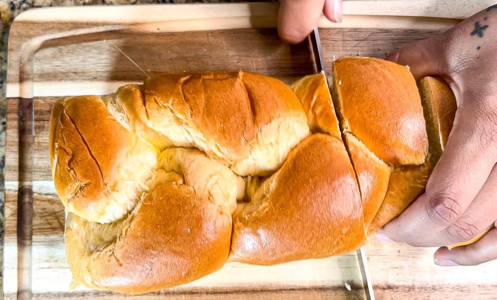 slicing a loaf of brioche bread to make Peach cobbler stuffed French toast