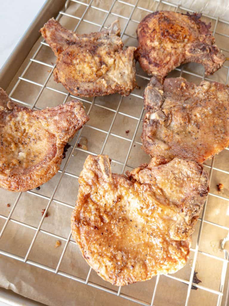 fried pork chops are sitting on a cooling rack to drain excess oil