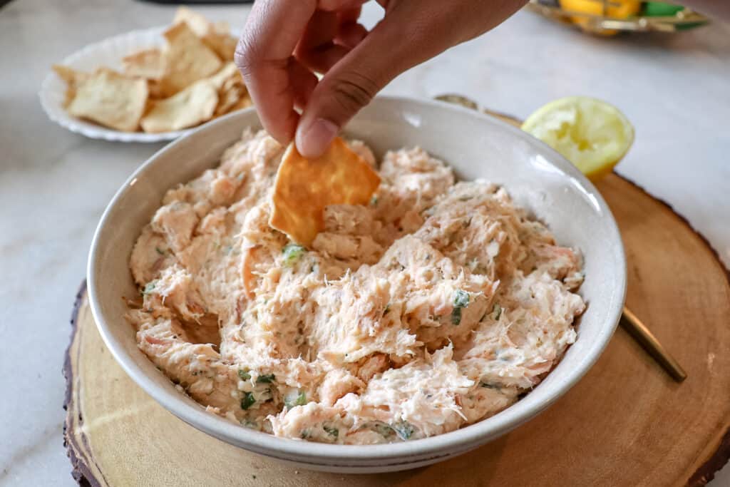 dipping a cracker into smoked salmon dip that is prepared in a bowl