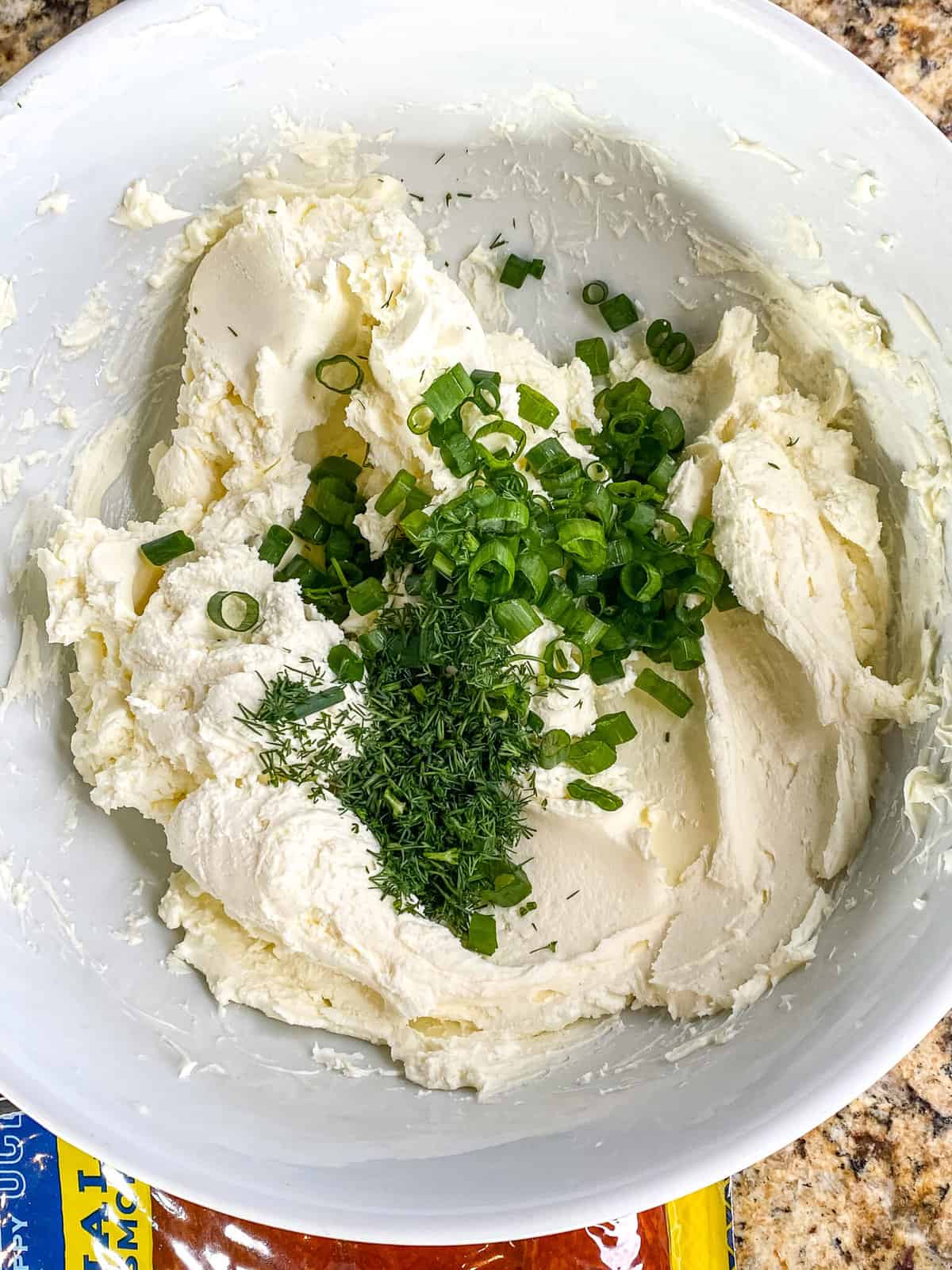 A bowl of mascarpone with chopped dill and green onions.