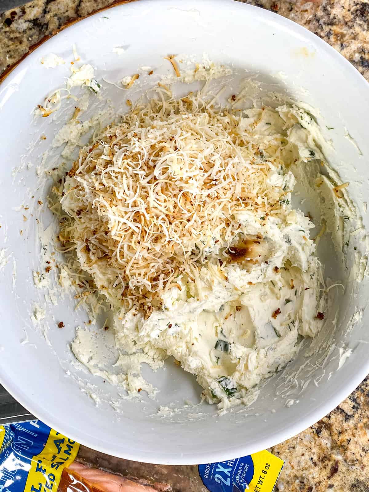 Shredded cheddar cheese added to a bowl of blended mascarpone cheese, green onions and dill.