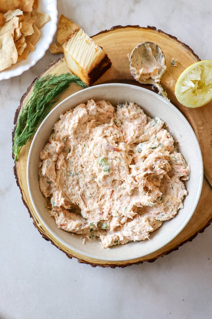 A bowl of smoked salmon dip garnished with dill, lemon and a bowl of crackers off to the side.