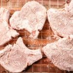 pork chops that have been covered in a seasoned flour breading are sitting on a cooling rack so that the breading can set