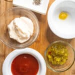 mayo, mustard, ketchup, sweet pickle relish, and salt and pepper in bowls on a cutting board