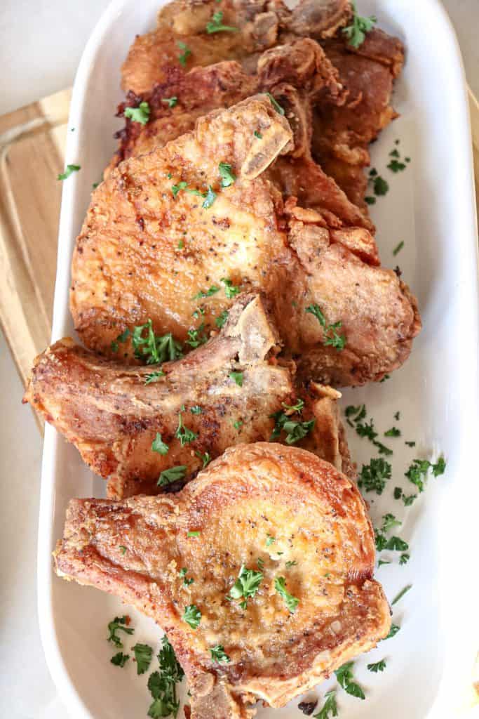 fried pork chops are served on a platter with chopped up parsley sprinkled over the top for garnishment