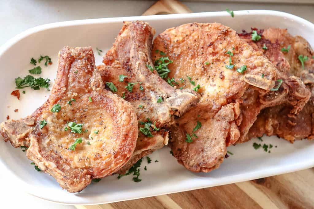 fried pork chops are served on a platter with chopped up parsley sprinkled over the top for garnishment