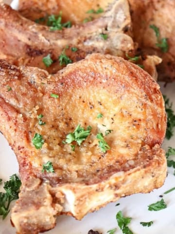 fried pork chops are served on a platter with chopped up parsley sprinkled over the top for garnishment