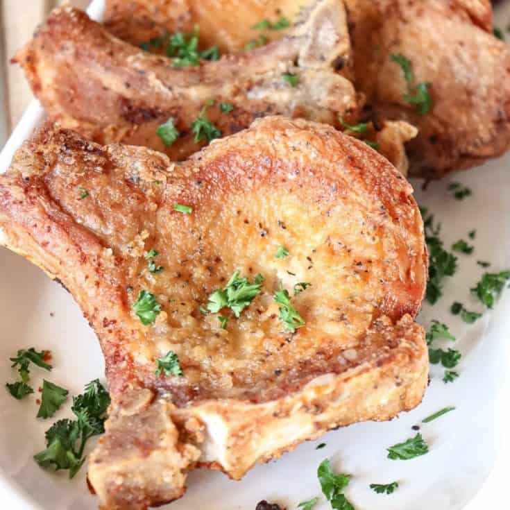 fried pork chops are served on a platter with chopped up parsley sprinkled over the top for garnishment