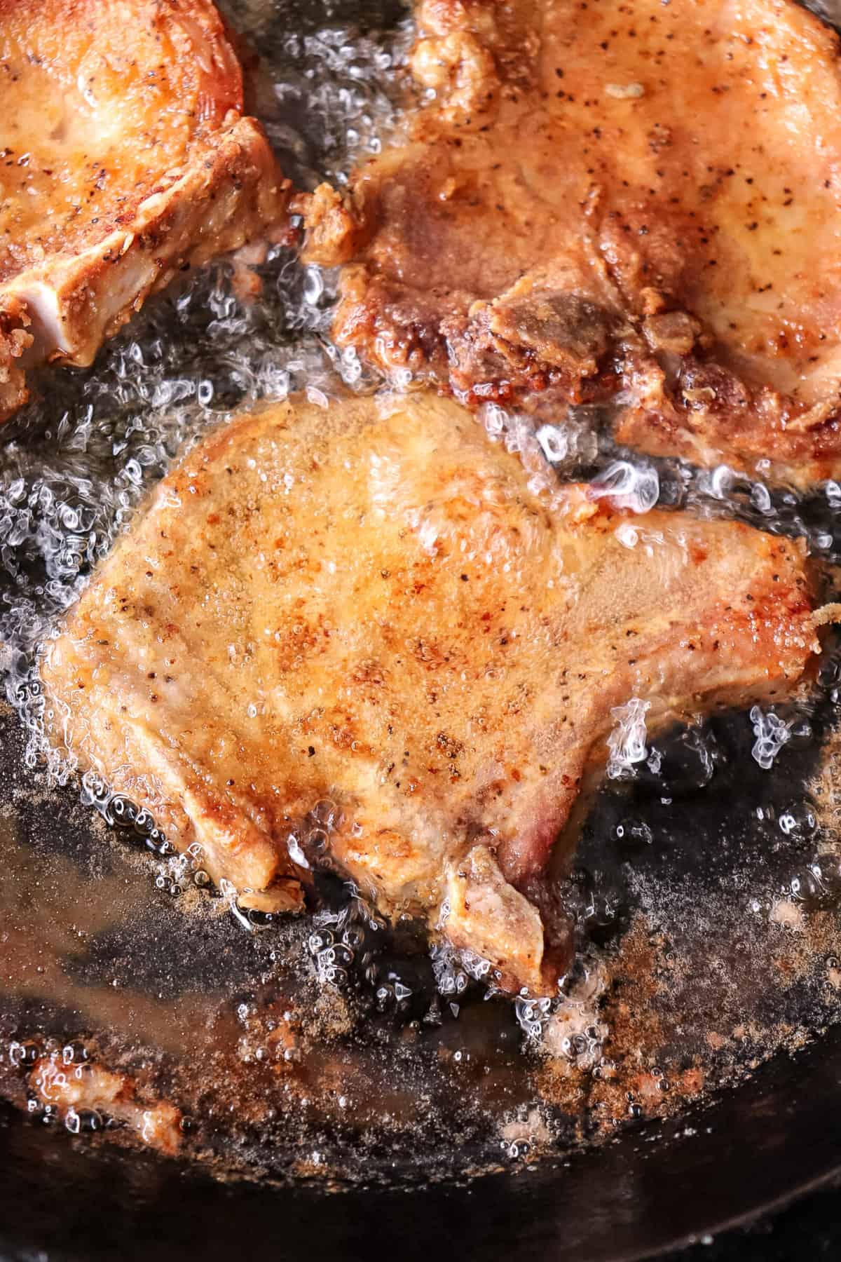 pork chops are frying in vegetable oil with bubbles visible from the frying process