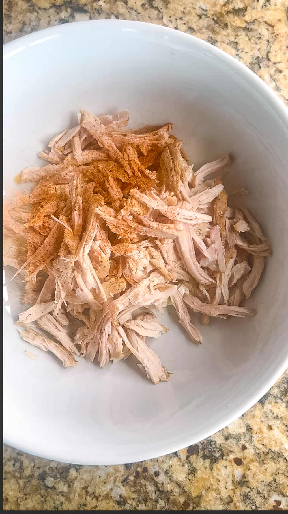 Seasoned salt spread over a bowl of shredded chicken and cream cheese.