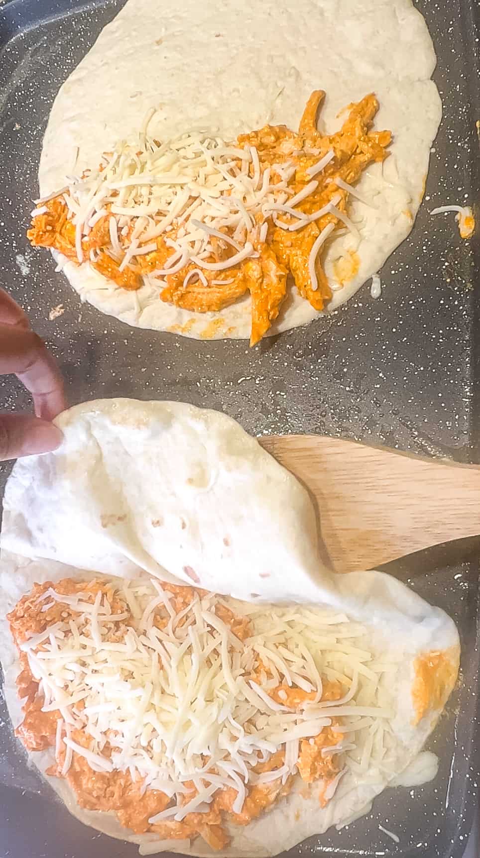 Close up shot of buffalo chicken mixture on half of a tortilla with shredded cheese on top.